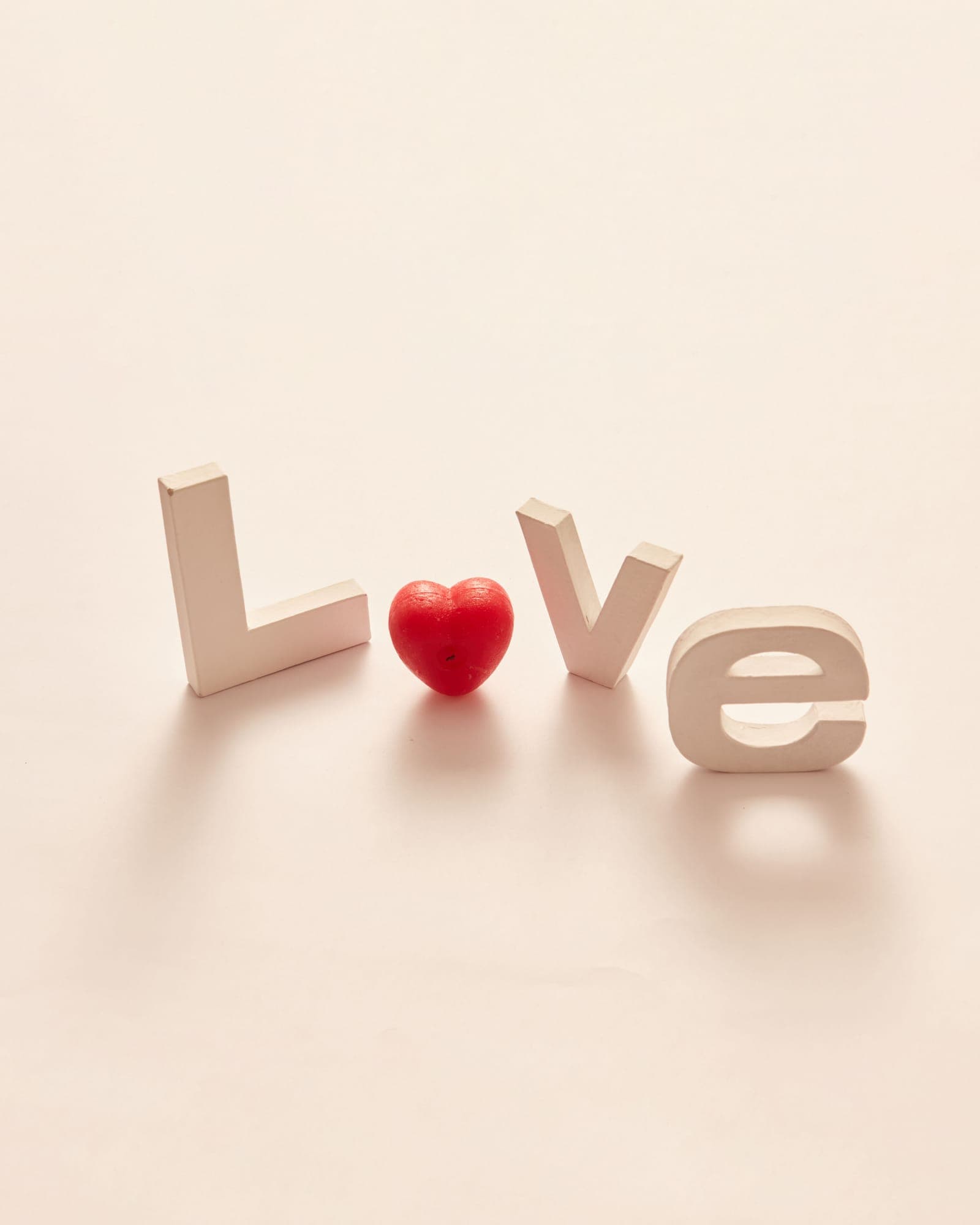 The word LOVE spelled in pale wooden letters on a cream background, a small red heart standing in for the O